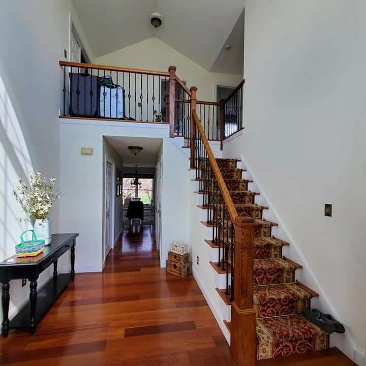 Foyer before the remodel — dated oak handrail, basket-twist iron balusters, and a patterned carpet runner on the treads
