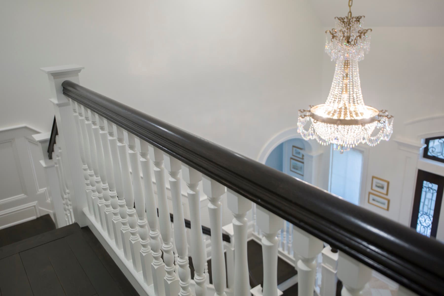 Ebonized handrail over white turned balusters on the Caruso balcony, crystal chandelier above the foyer — Caruso residence