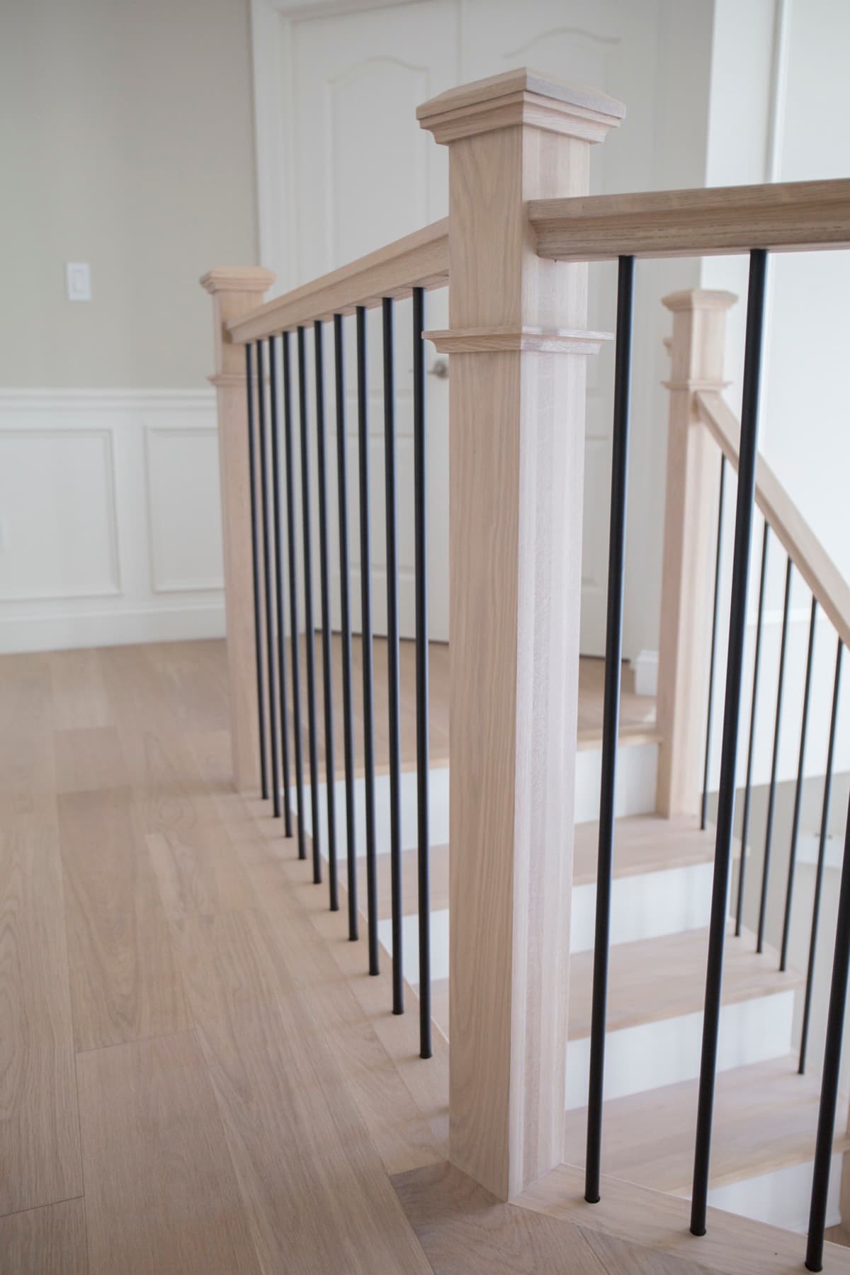 Clean modern staircase — natural white-oak newel and handrail with slim satin-black iron balusters over light oak floors — Modern White Oak project