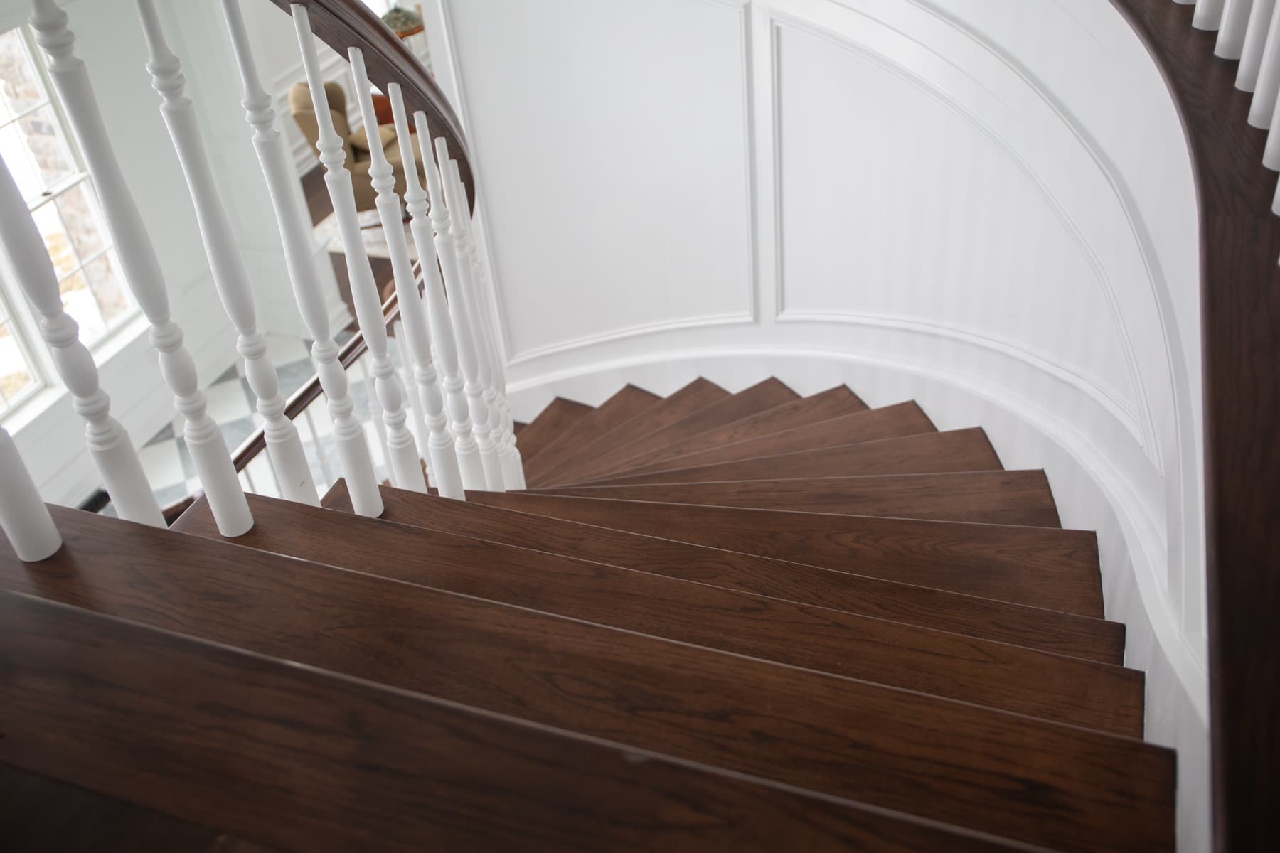 Curved walnut treads winding past white turned balusters and raised-panel wainscoting — Rambo residence, Lehigh Valley